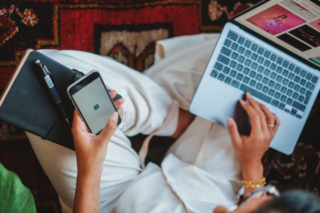 Person seated indoors reviewing an online listing on a smartphone beside a notebook