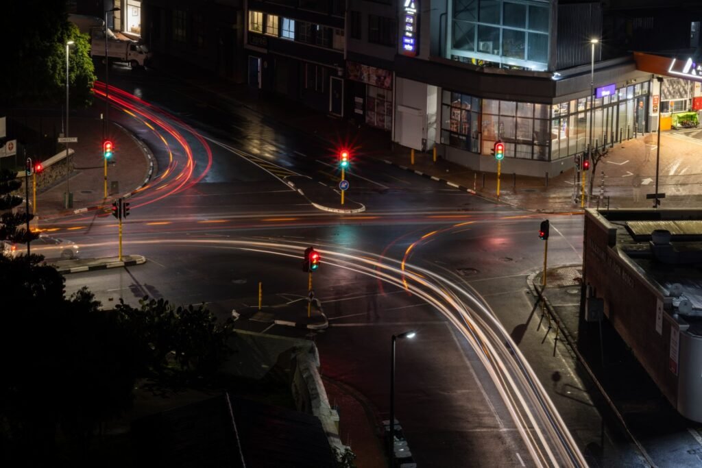 An aerial view of an illuminated city intersection at night, showcasing vibrant light trails from passing vehicles.