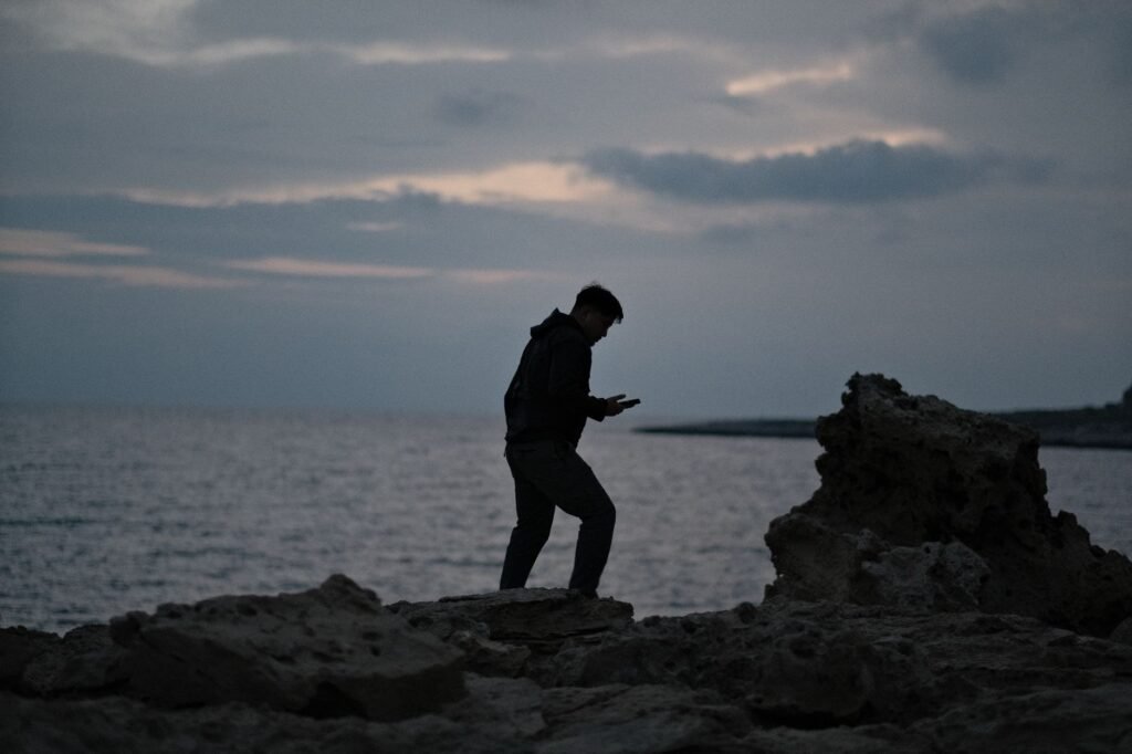 A person checking their phone beside a car at dusk on a quiet road