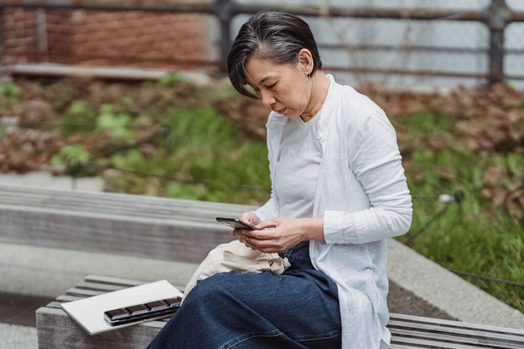 Person seated outdoors reading a listing on a smartphone in soft daylight