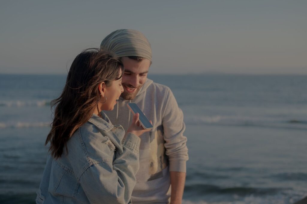 A couple sitting together outdoors and talking while looking at a phone