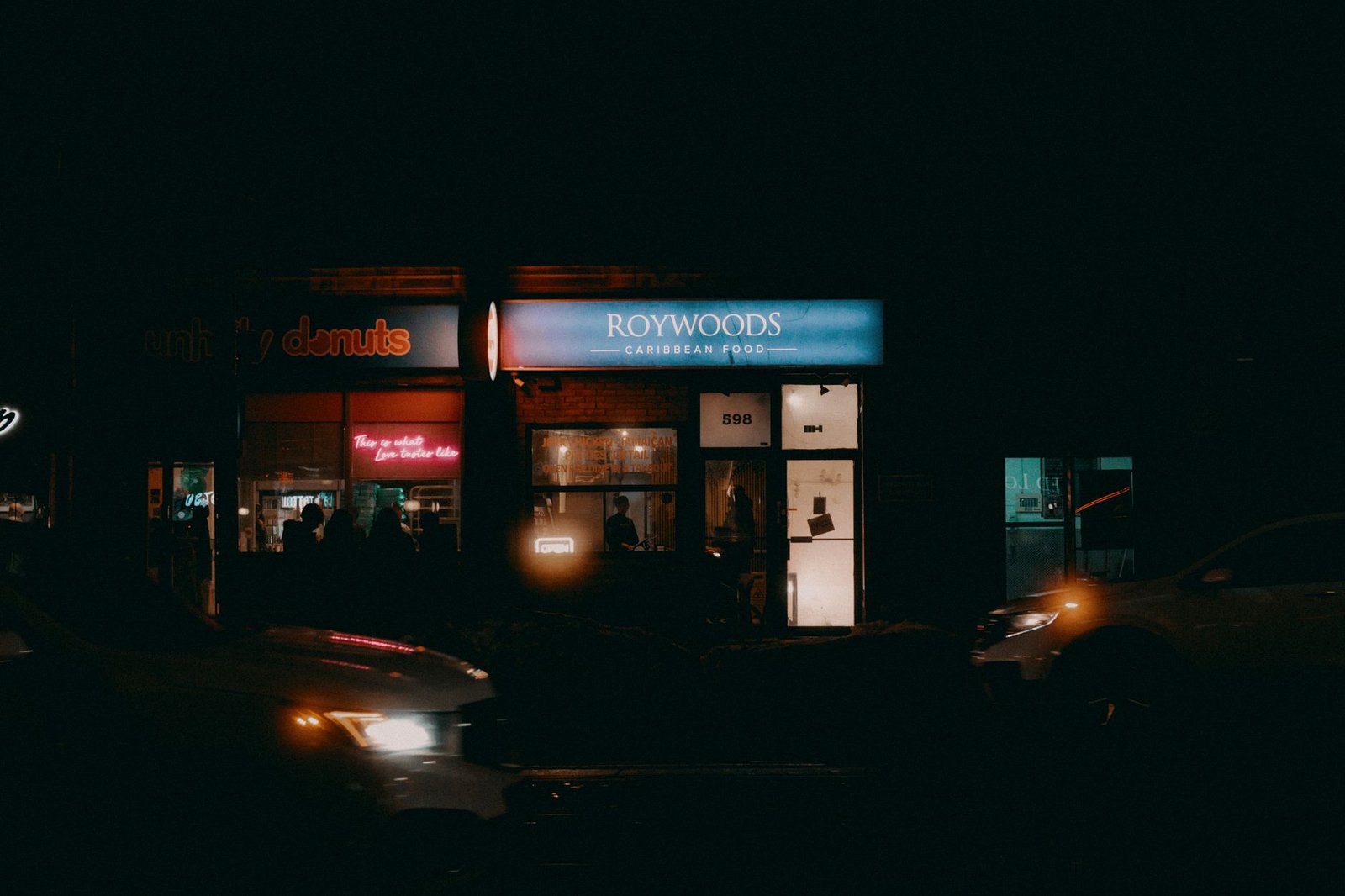 A vibrant nighttime view of a street with illuminated shopfronts and neon signs.