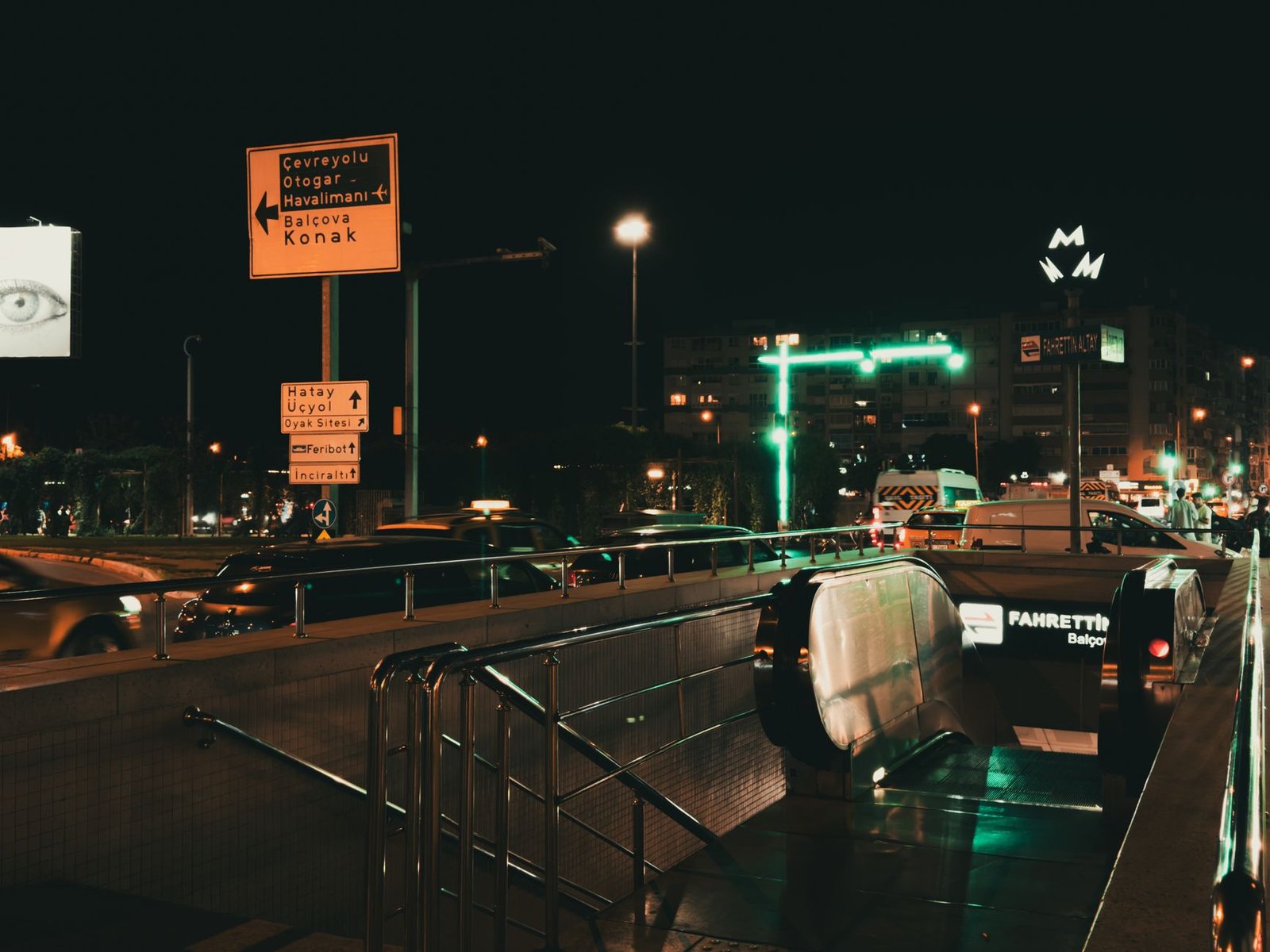 Busy nighttime street scene in İzmir, Türkiye with traffic and subway entrance.