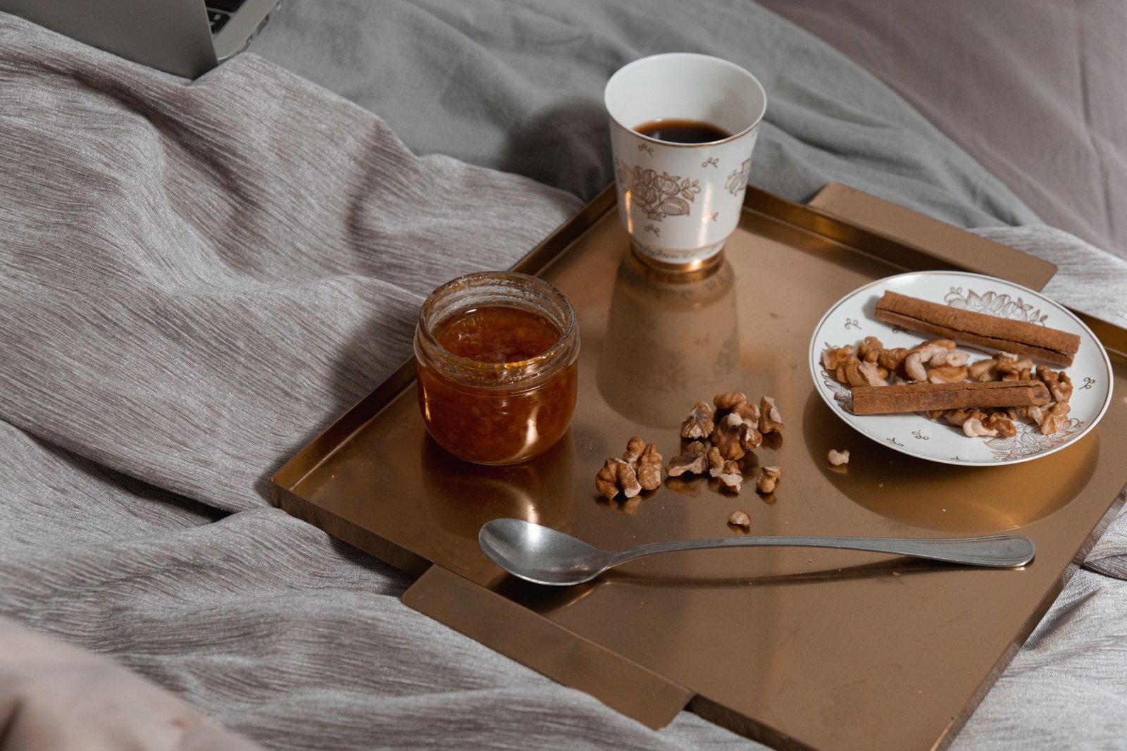 A comforting breakfast setup with coffee, nuts, and jam on a tray in bed, perfect for a cozy morning.