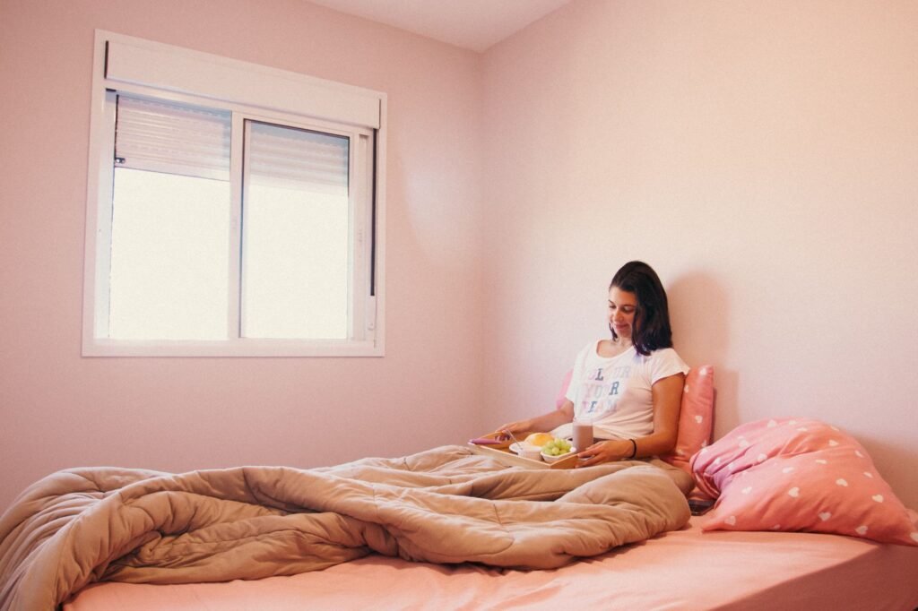 A woman relaxes with breakfast in bed in a cozy pink room, enjoying a peaceful morning.