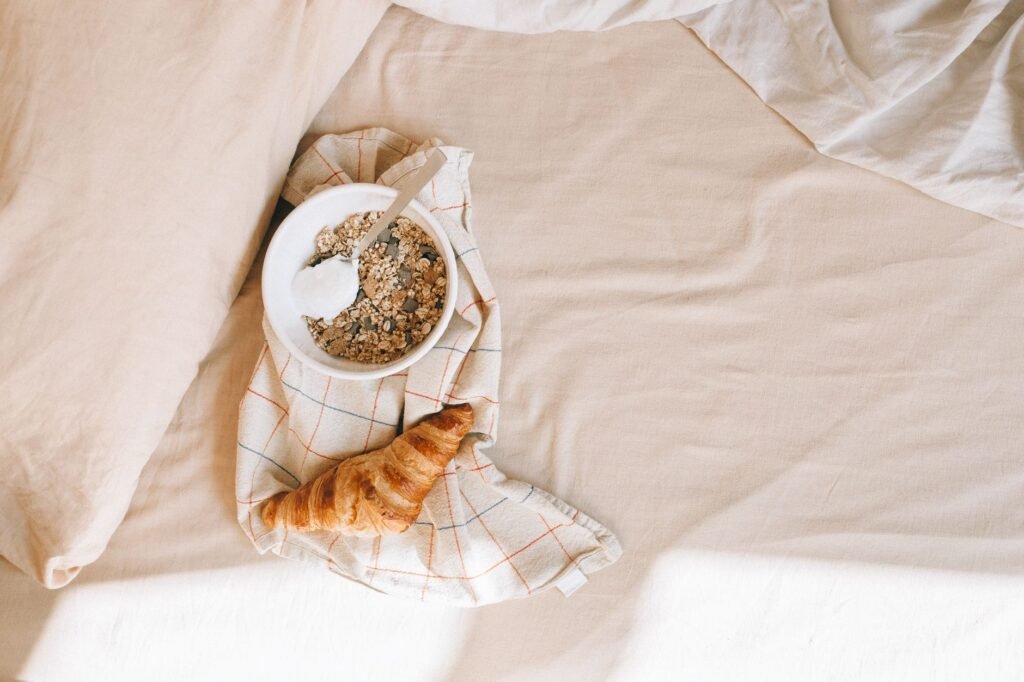 A cozy breakfast setup with a bowl of cereal and croissant on a bed for a relaxing morning.