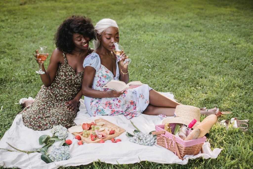 Two women enjoying a picnic with wine and books on a sunny day in the park.