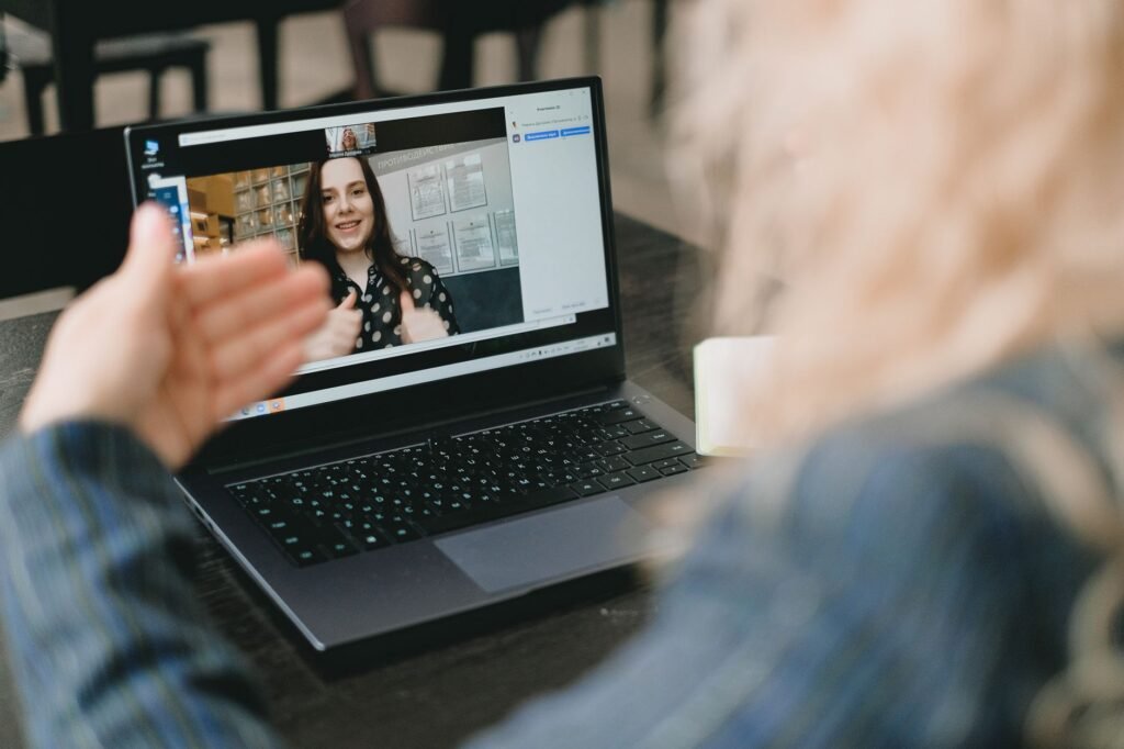 Crop anonymous businesswoman with blond hair in formal clothes sitting at table and having video call via laptop with female