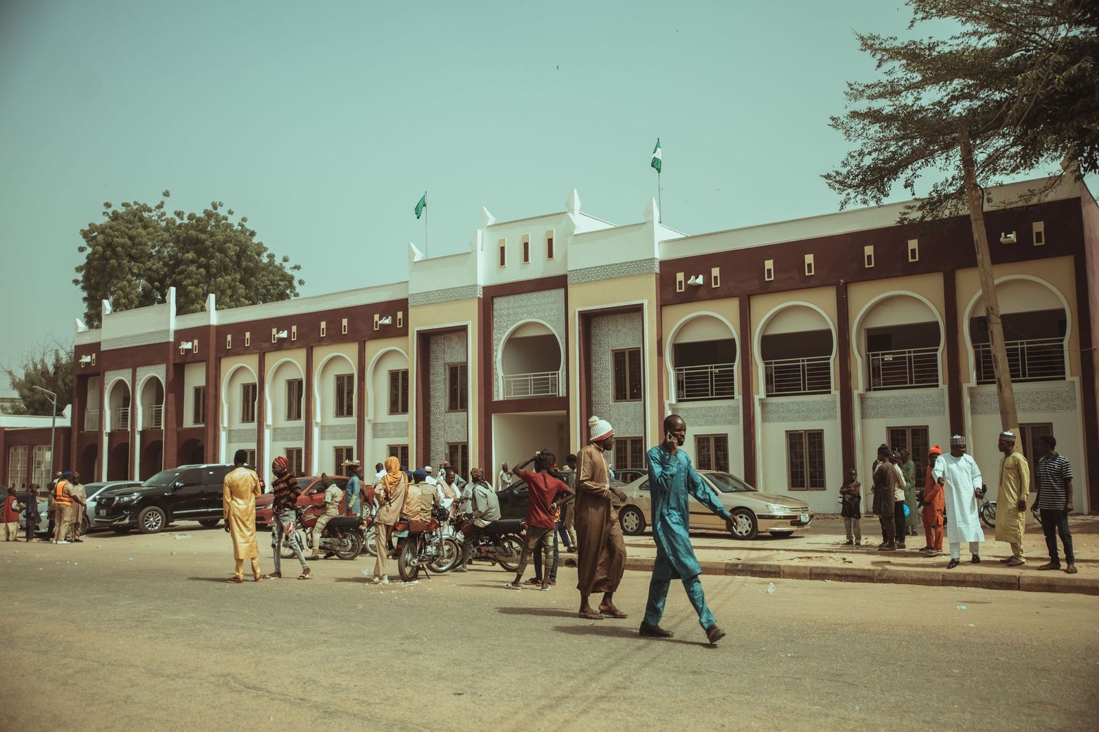 People gather outside a traditional building with arches in a vibrant street scene.