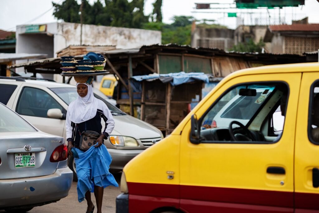 A street vendor skillfully balances goods on her head in a busy Oyo street.