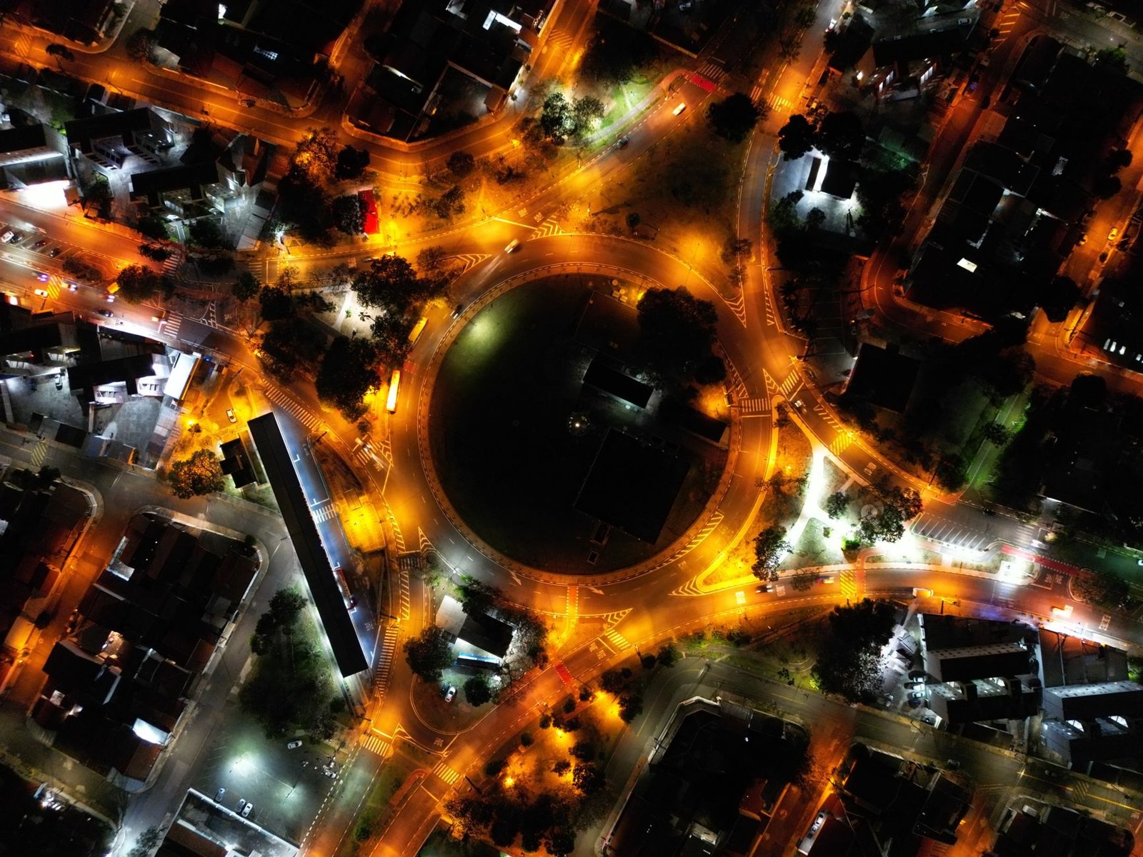 A stunning aerial view of a city roundabout lit up at night with vibrant streetlights and traffic.
