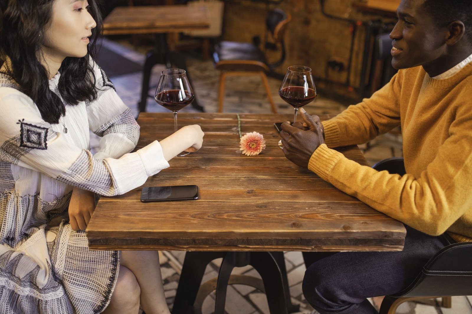 Interracial couple enjoying a romantic date with wine in a cozy café setting.