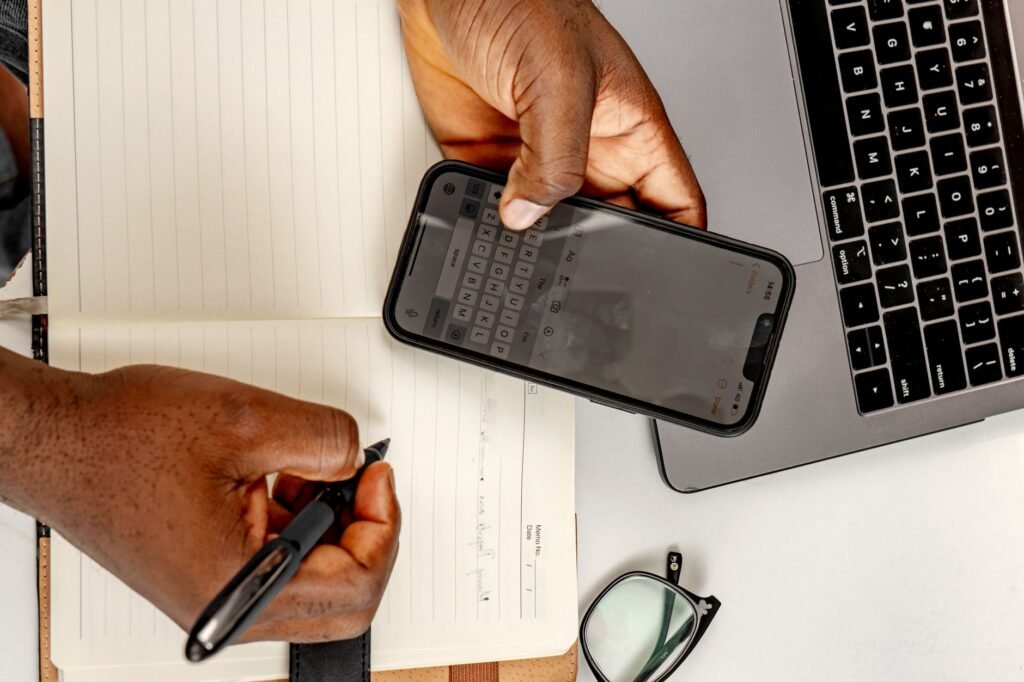 Person typing a message on a phone beside a notebook on a wooden table