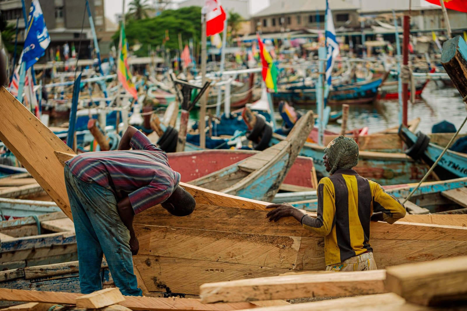 Fishermen repairing wooden boats at Tema harbor, highlighting traditional craftsmanship in Ghana.