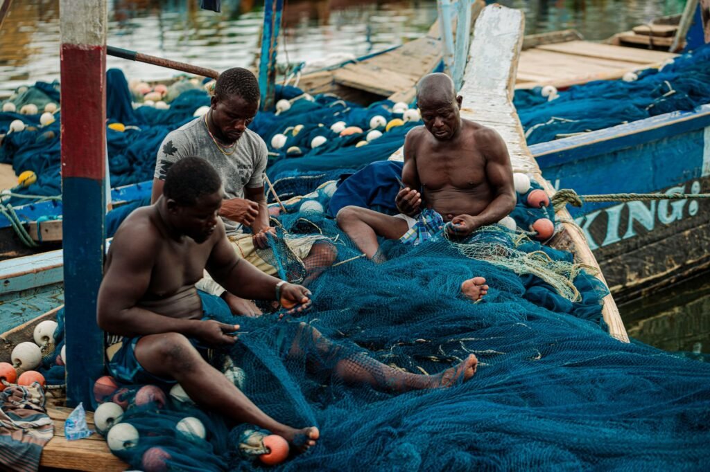 Three African fishermen repairing fishing nets on a traditional boat in Tema, Ghana.