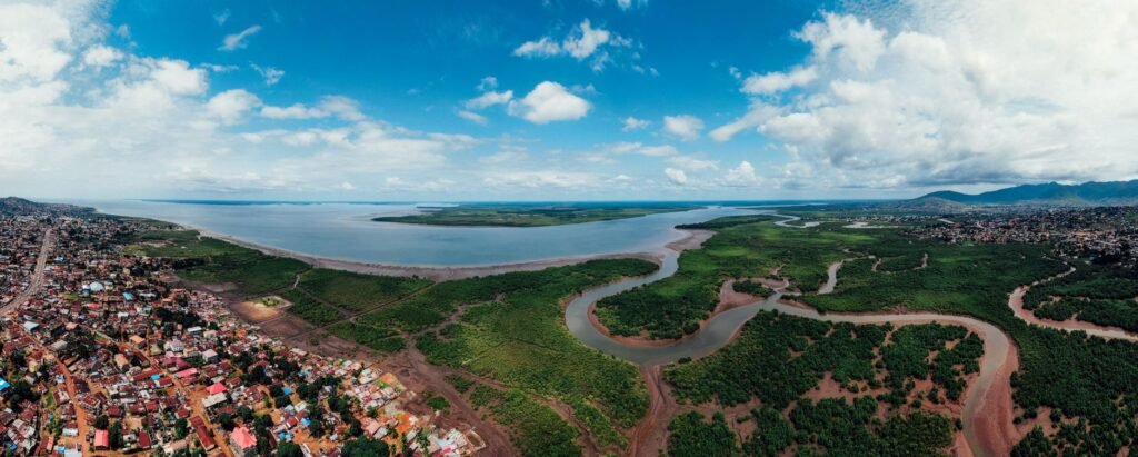 Panoramic aerial view of a coastal city with lush greenery, winding river, and expansive blue sky.
