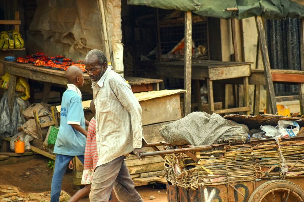 An elderly man and boy navigate a bustling market street with various goods and vibrant colors.