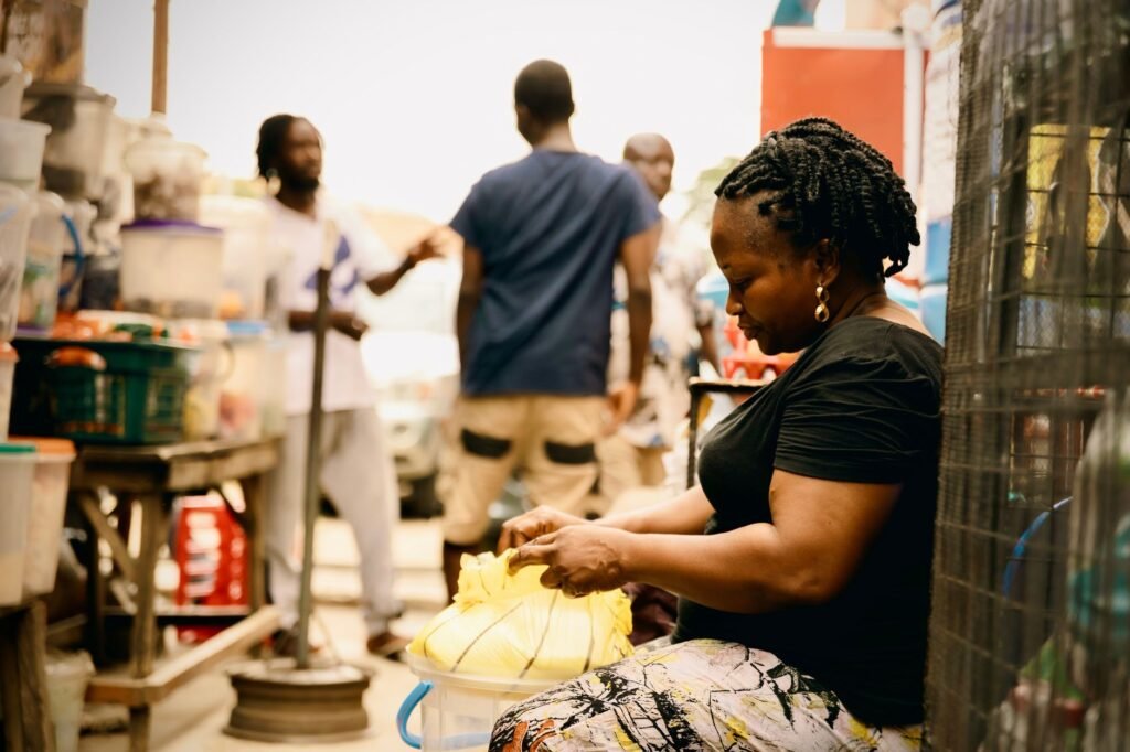 A woman prepares goods in a bustling street market environment, showcasing daily trade and interactions.