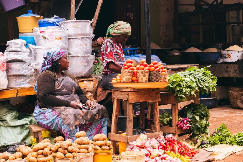 Colorful market scene in Jos, Nigeria showcasing women selling fresh produce with vibrant vegetables and baskets.