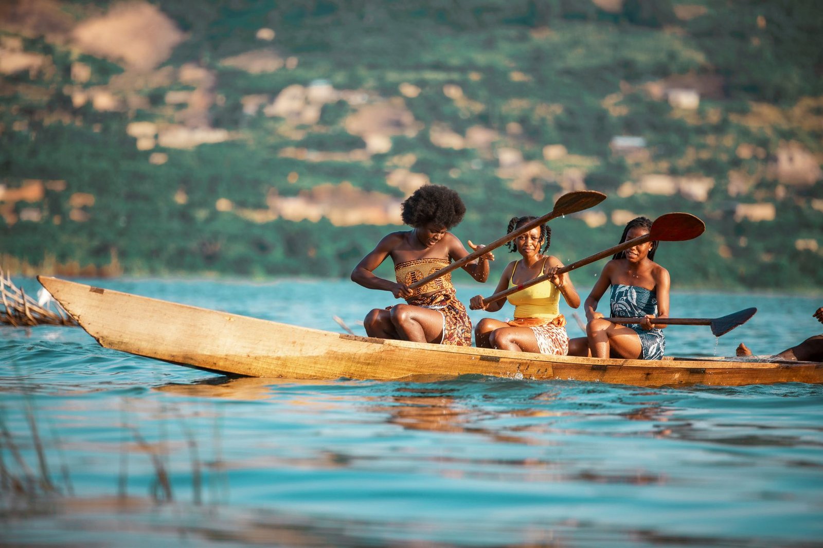 Three women paddle a wooden canoe on a scenic river in Accra, Ghana.