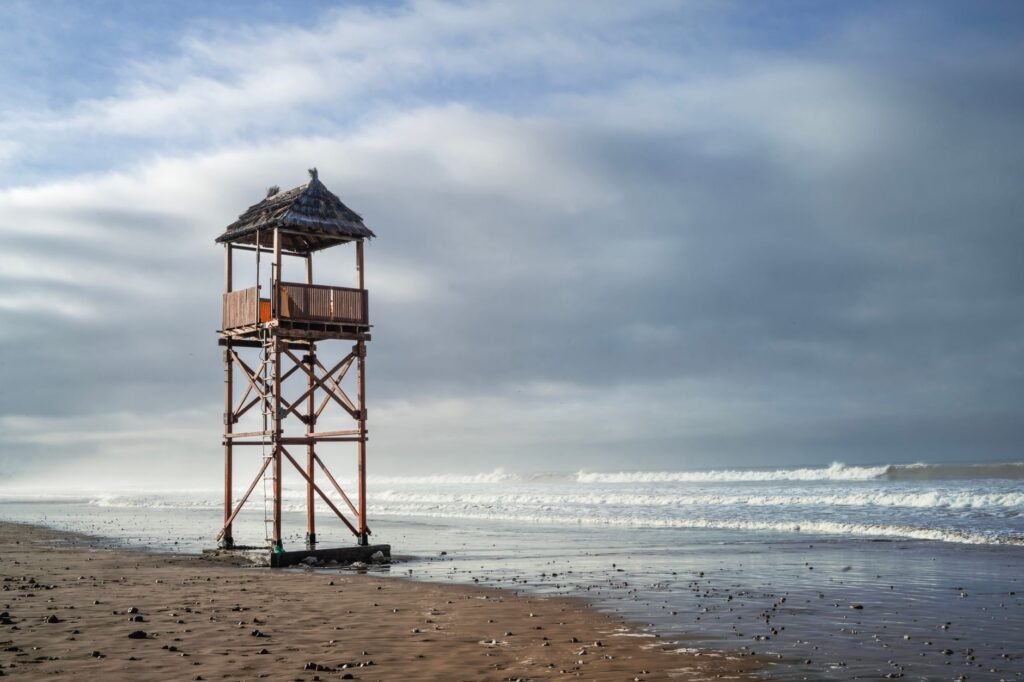 A solitary lifeguard tower stands on a deserted beach in Agadir, Morocco under a cloudy sky.