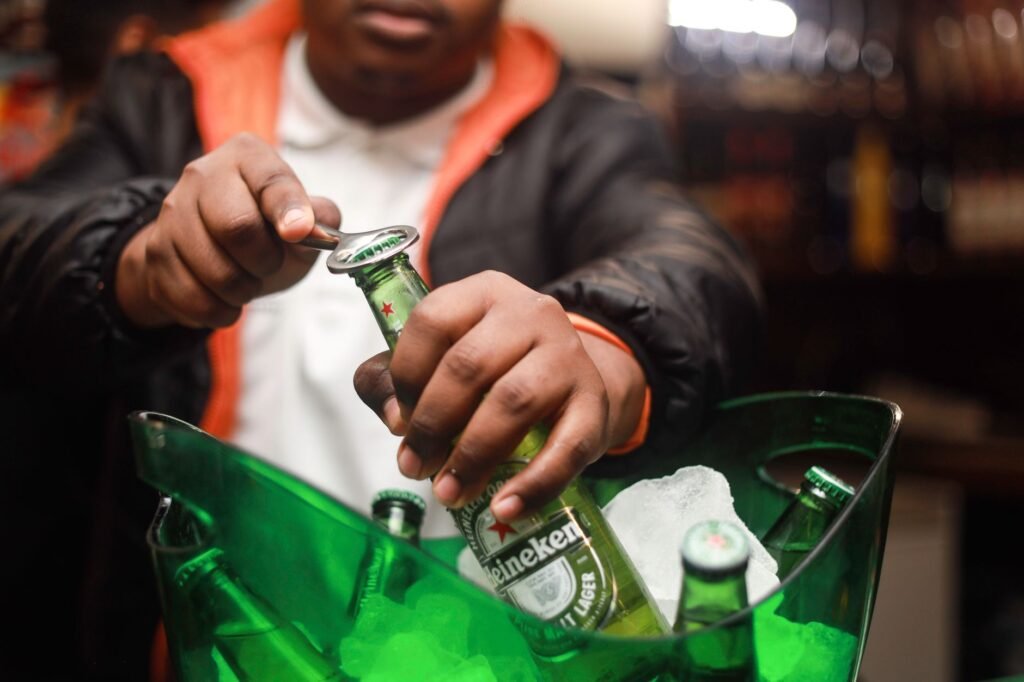 A man opens a Heineken beer bottle from a bucket of ice indoors in South Africa.