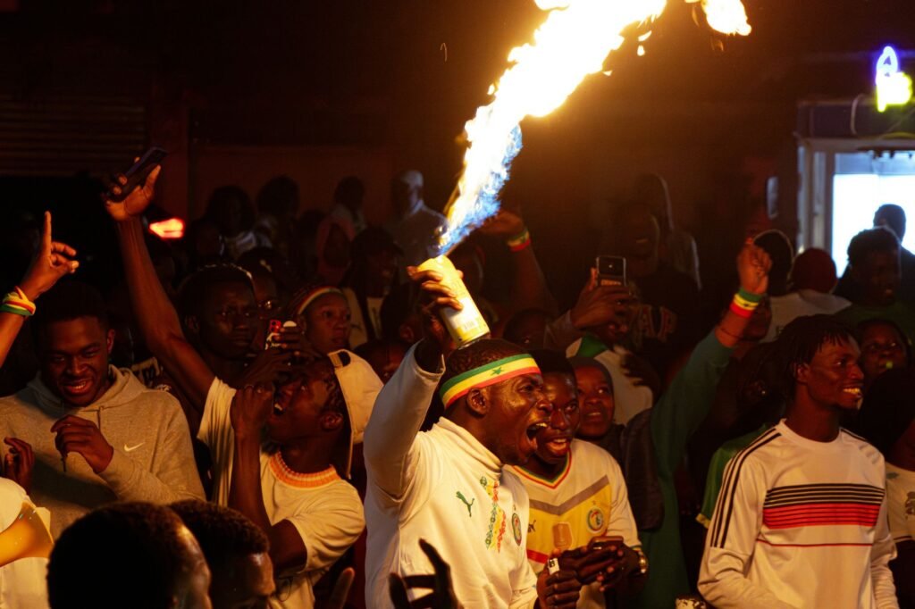 A lively night celebration in Senegal with a man holding a firework as people cheer around him.