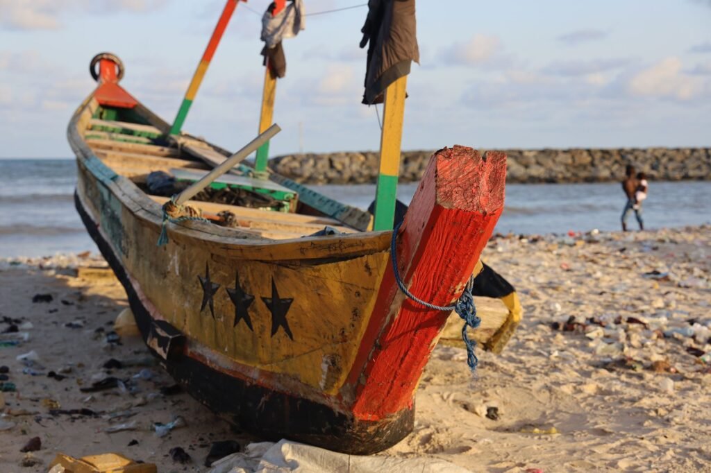 Colorful fishing boat on a sandy beach in Accra, Ghana, with the ocean backdrop.