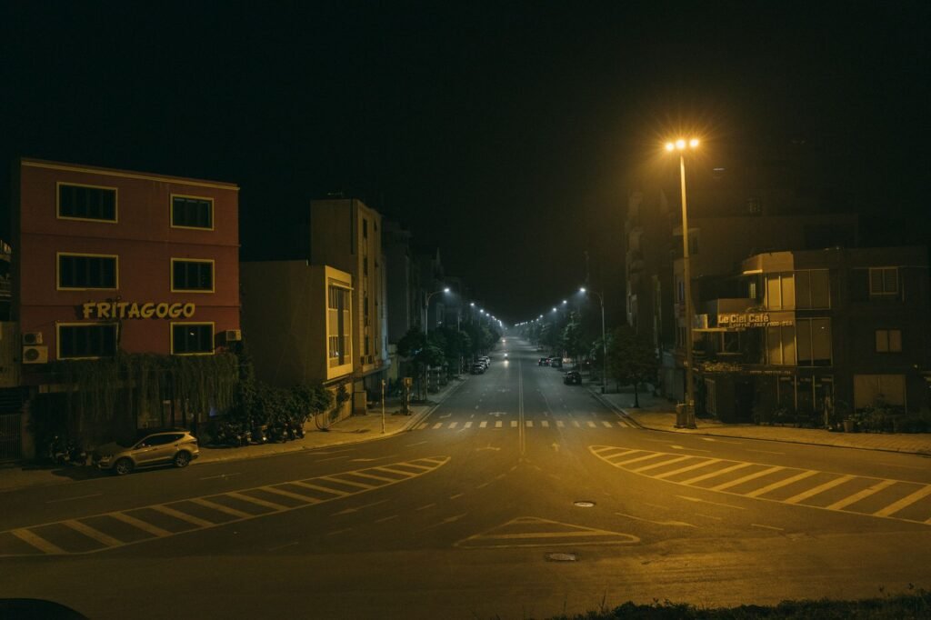 Deserted urban street at night with illuminated streetlights and empty pedestrian lanes.