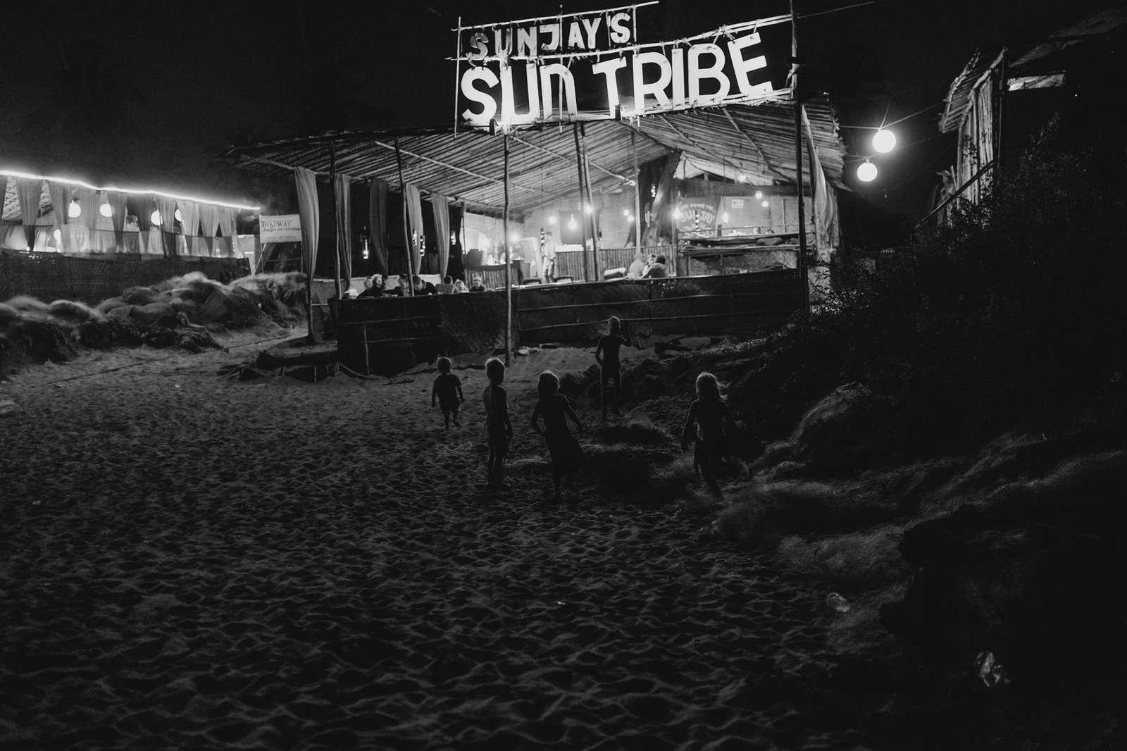 Children play under a lit beach bar at night, offering a vibrant Goa beach nightlife vibe.