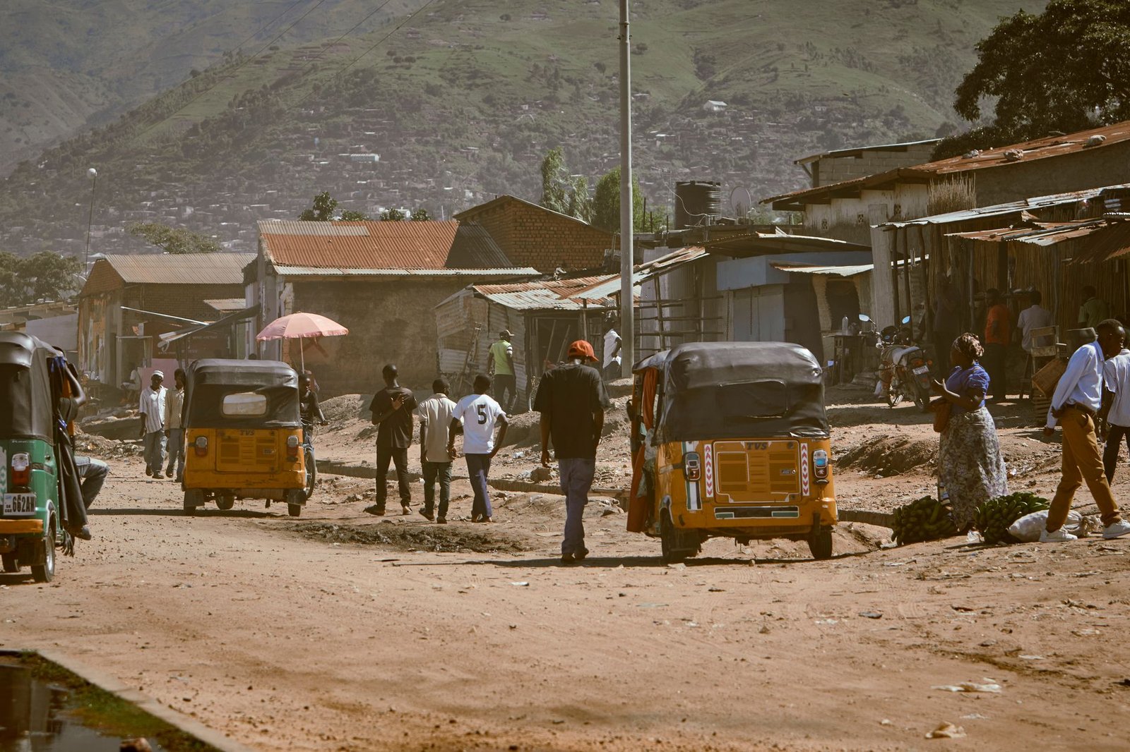 Street view with rickshaws and locals against a scenic mountain backdrop.