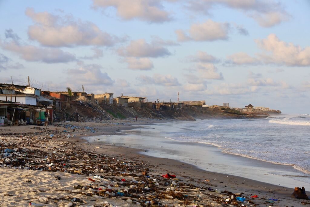 Coastal pollution littering a beach in Accra, Ghana, with buildings in the background.