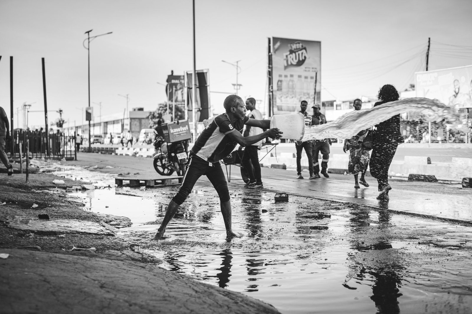 Black and white photo of a man splashing water on urban street, creating dynamic motion.