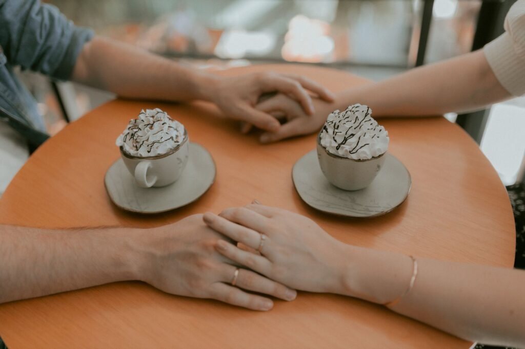 Couple holding hands over hot chocolate at a cozy cafe setting.