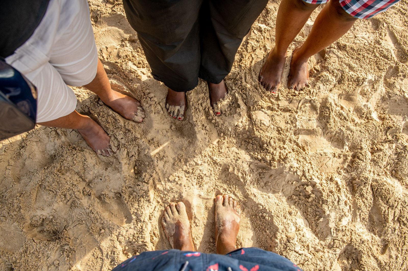 Feet of diverse individuals enjoying a sunny day on a sandy beach in Accra, Ghana.