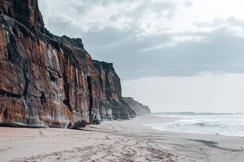 Stunning view of eroded cliffs along a serene sandy beach under a cloudy sky.