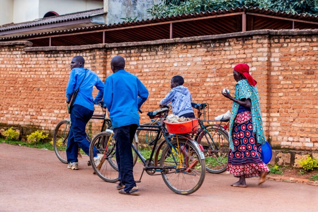 A family strolls with bicycles on a street beside a brick wall, showcasing vibrant attire.