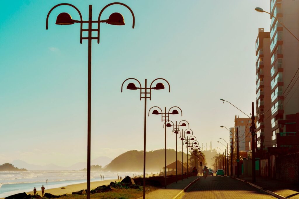 Scenic view of a coastal road lined with modern lampposts and buildings at sunrise.
