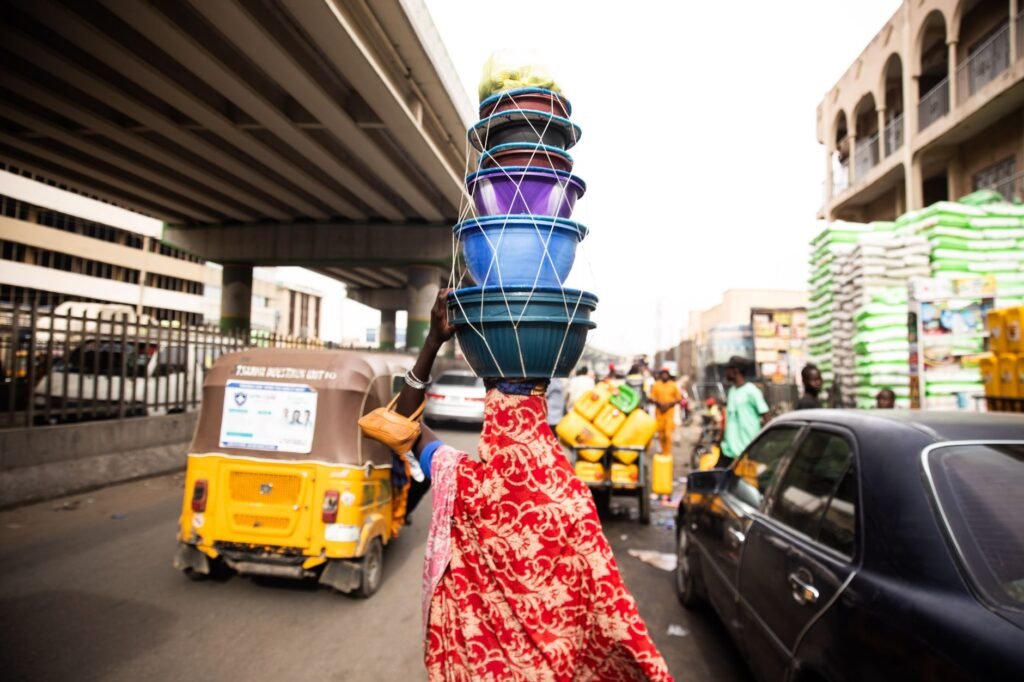A street vendor skillfully balances colorful bowls in a busy Kano market.