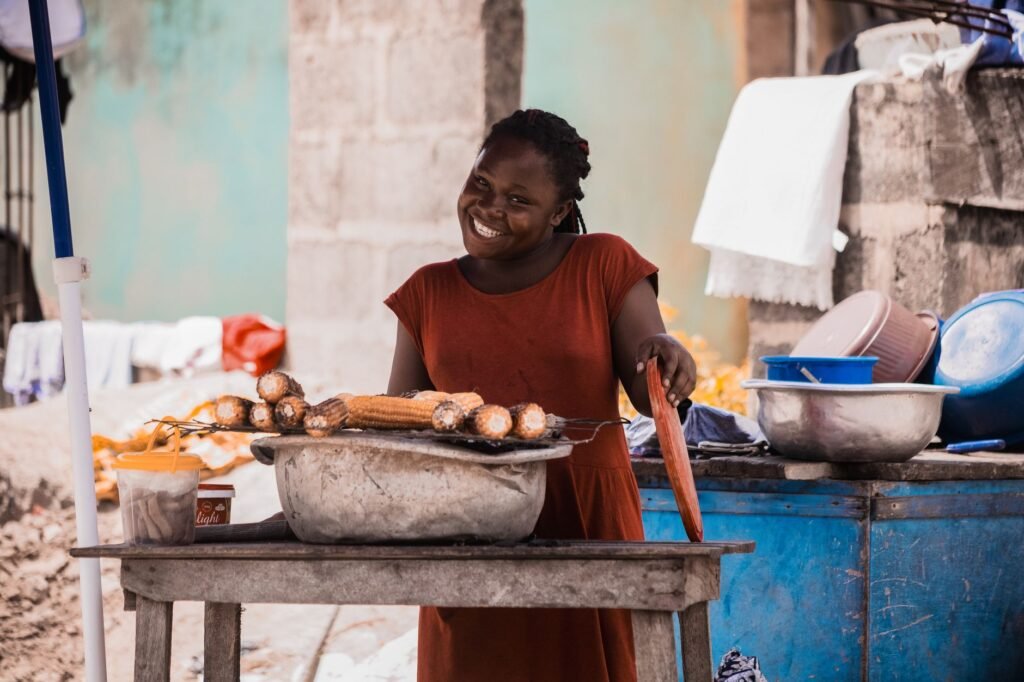 A woman vendor in Takoradi, Ghana, joyfully sells roasted corn outdoors.