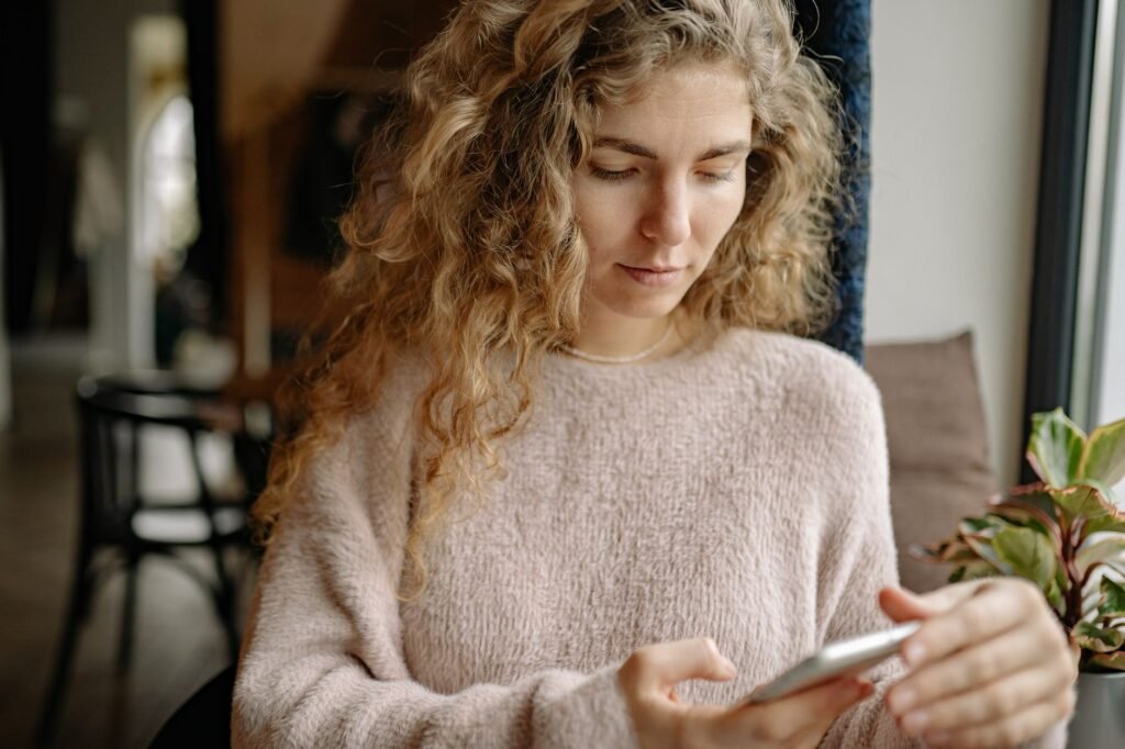 Person typing a short, thoughtful message on a smartphone beside a window in soft afternoon light