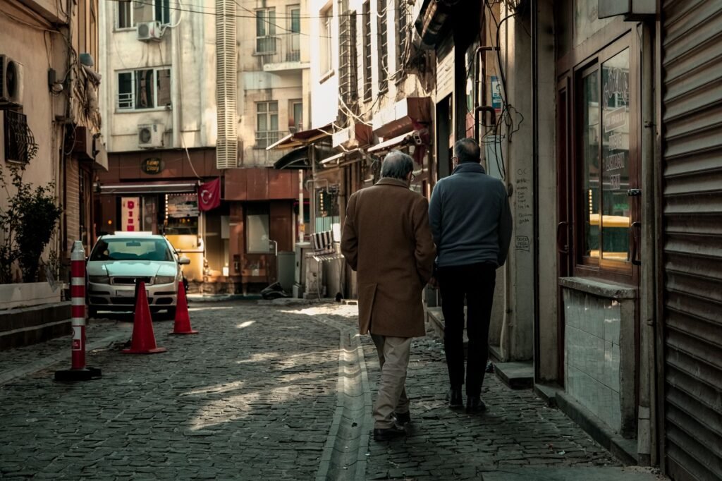 Two adults walking and talking along a quiet street in a small Ghanaian town as streetlights come on