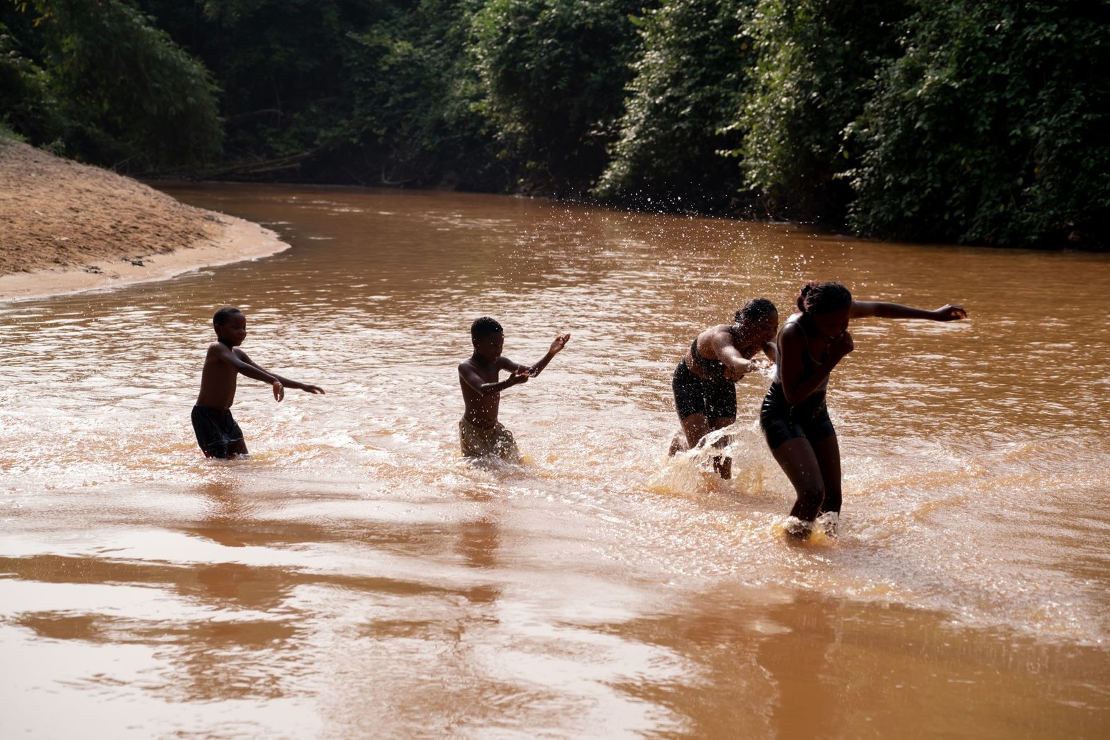 Joyful children playing and splashing in a river in Ghana, surrounded by lush greenery.