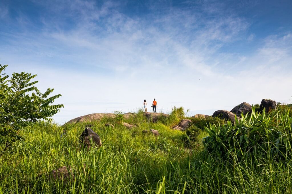 A scenic outdoor landscape with two individuals hiking on a grassy hill under a blue sky in Kon Tum, Vietnam.