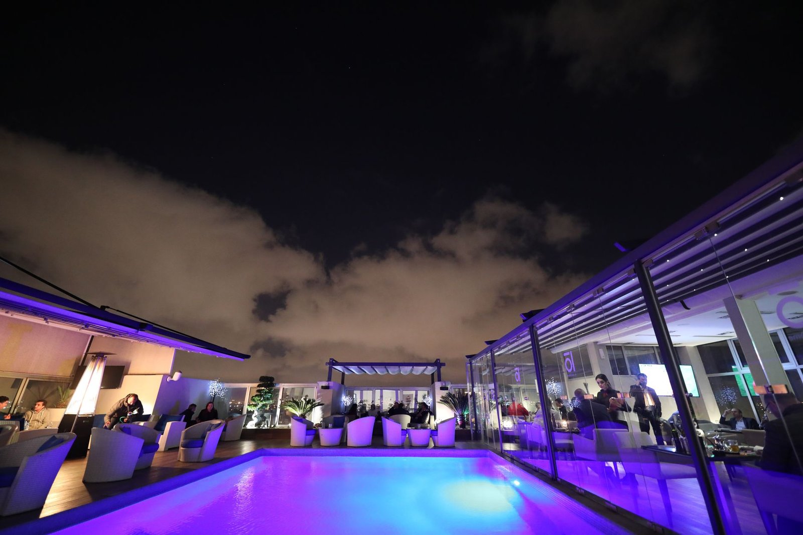 A vibrant rooftop lounge with a glowing pool under a starlit night sky, perfect for relaxation.