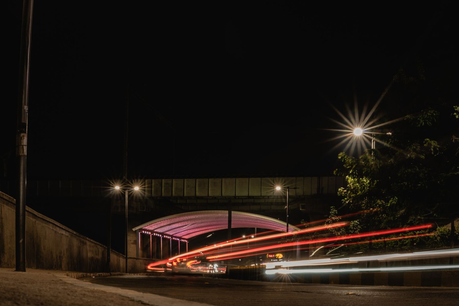 Captivating long exposure shot of city street at night with vibrant light trails and illuminated bridge.