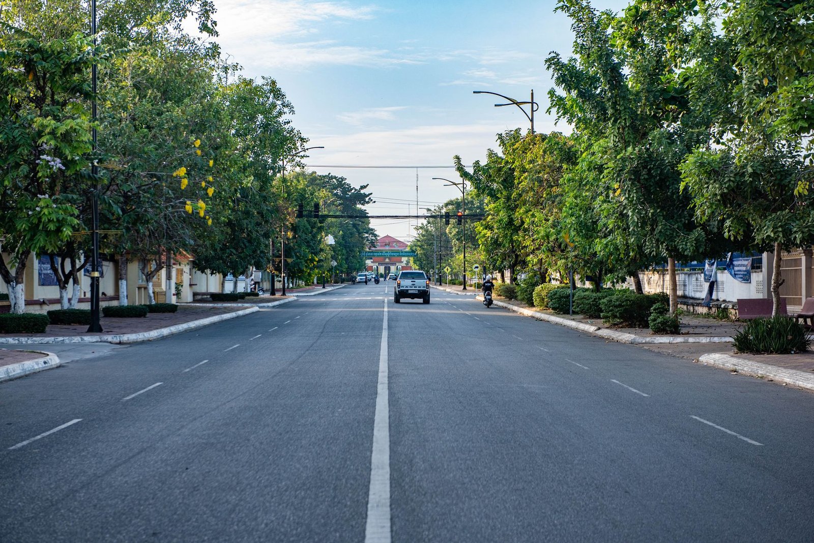 Serene view of a tree-lined street in Krong Kampong Cham, Cambodia, with few vehicles.