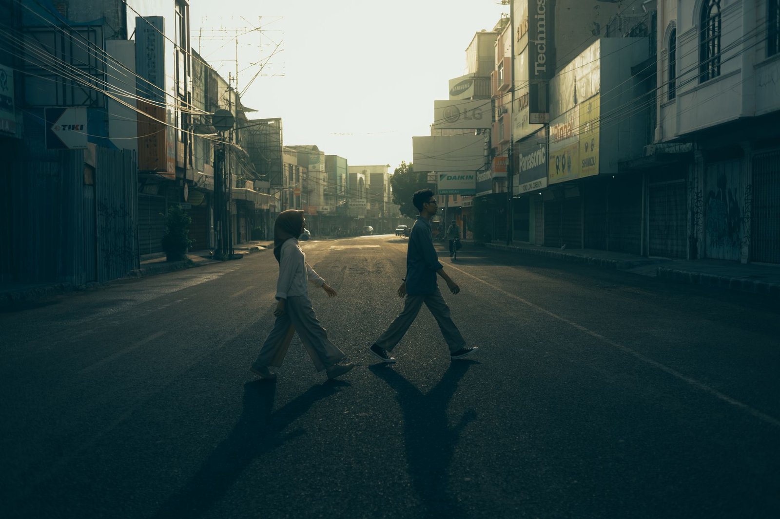 A couple strolls on an empty street in Cirebon, Indonesia at sunrise, evoking romance and tranquility.