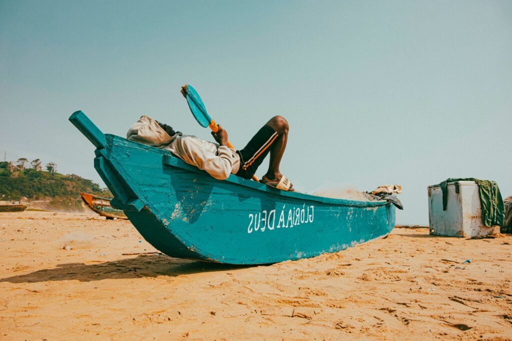 A man relaxes on a blue boat on a sandy beach, capturing a serene coastal atmosphere.