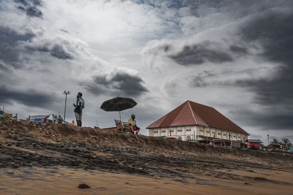 A stormy beach scene with people and a distinct building, showcasing dramatic clouds for a moody feel.